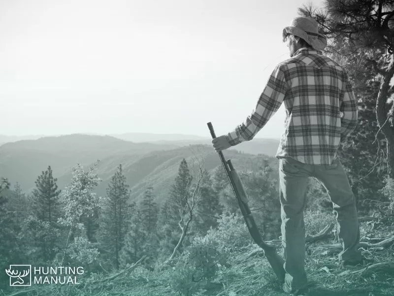 hunter standing on hill top with rifle in hand